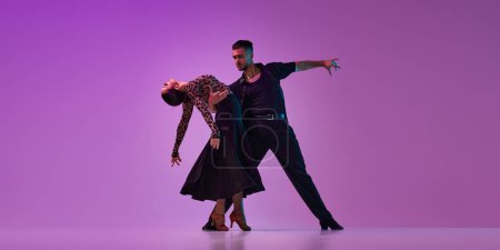 Téléchargez les photos : Young talented man and woman, professional dancers in stylish costumes performing tango on purple background on neon lights. Concept of , lifestyle, action, beauty of movements, emotions, fashion, art - en image libre de droit