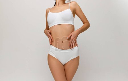 Foto de Dieting. Cropped image of slim healthy female body, breast, belly over grey studio background. Model posing in white underwear. Concept of body and skin care, fitness, natural beauty, health, wellness - Imagen libre de derechos