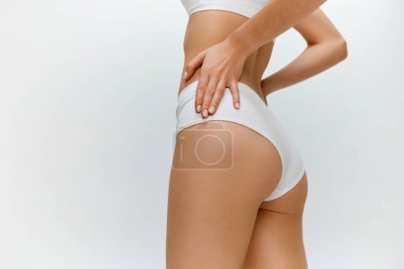 Téléchargez les photos : Anti-cellulite. Cropped image of fit healthy female body. buttocks on grey studio background. Model posing in white underwear. Concept of body and skin care, fitness, natural beauty, health, wellness. - en image libre de droit