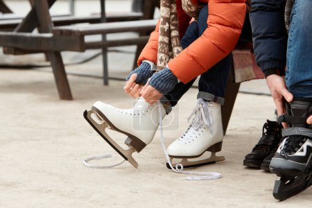 Téléchargez les photos : Image recadrée d'une femme attachant des lacets sur des patins, se préparant à patiner sur une patinoire. Favoriser le passe-temps et l'activité hivernale. Arène extérieure. Loisirs, sports d'hiver, vacances, plaisir, relation, émotions concept - en image libre de droit