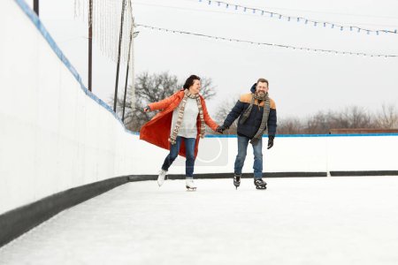 Photo for Happiness, positive mood. Middle-aged couple skating on open air ice rink in warm winter day. Concept of leisure activity, winter hobby and sport, vacation, fun, relationship, emotions. - Royalty Free Image