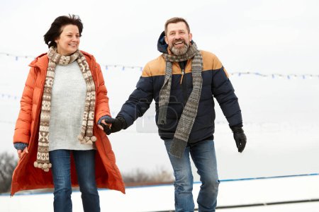 Photo for Middle-aged smiling happy people, man and woman spending time on open ice rink in winter day. Concept of leisure activity, winter hobby and sport, vacation, fun, relationship, emotions. - Royalty Free Image