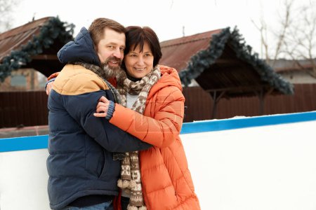 Photo for Middle-aged people, happy couple, man and woman visiting open-air ice rink in winter day. Hugs, smiles. Concept of leisure activity, winter hobby and sport, vacation, fun, relationship, emotions. - Royalty Free Image