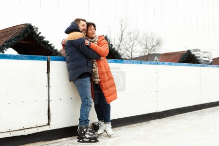Photo for Middle-aged people, happy couple, man and woman visiting open-air ice rink in winter day, hugging, smiling. Concept of leisure activity, winter hobby and sport, vacation, fun, relationship, emotions. - Royalty Free Image
