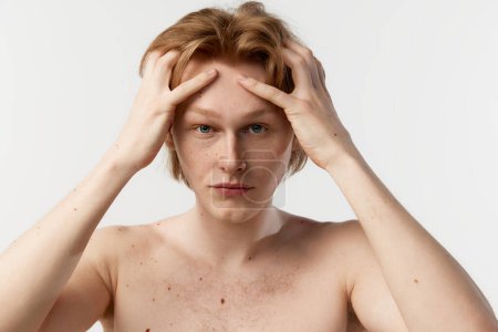 Téléchargez les photos : Head massage. Getting ready after shower. Portrait of young redhead man posing shirtless over grey studio background. Concept of mens health, body and skin care, hygiene and male cosmetology - en image libre de droit