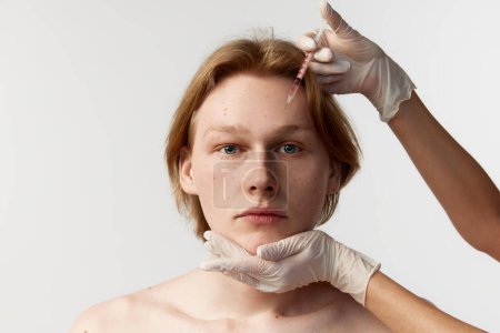 Foto de Reducing forehead wrinkles with botox. Young redhead man having cosmetological injections. Male model posing against grey background. Mens health, cosmetology, plastic surgery, kin care, medicine - Imagen libre de derechos