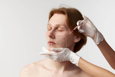 Photo for Botox in cheeks. Face lifting. Young redhead man having cosmetological injections. Male model posing against grey background. Mens health, cosmetology, plastic surgery, skin care, hygiene, medicine - Royalty Free Image