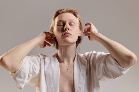 Foto de Portrait of young redhead man posing in white shirt over grey studio background. Casual mans fashion, comfort and wellness. Concept of mens health, body and skin care, hygiene and male cosmetology - Imagen libre de derechos