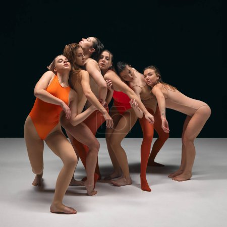 Foto de Danza experimental. Grupo de jóvenes hermosas chicas flexibles en trajes de cuerpo que realizan, bailando desprecio sobre fondo de estudio negro. Concepto de arte, movimiento, juventud, moda, estilo de vida artístico - Imagen libre de derechos