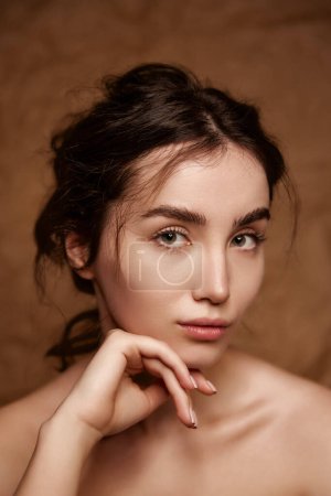 Téléchargez les photos : Beautiful young brunette girl with curly hair, nude makeup on perfect healthy skin posing over brown studio background. Concept of natural beauty, skincare, cosmetology, plastic surgery, health - en image libre de droit