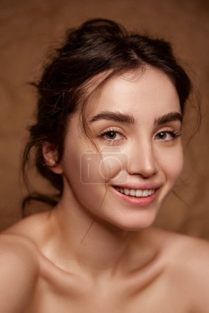 Photo for Tenderness and purity. Beautiful smiling young brunette girl with clear healthy skin posing over brown studio background. Concept of natural beauty, skincare, cosmetology, plastic surgery, health, spa - Royalty Free Image