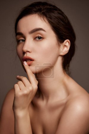Foto de Perfect skin and natural make-up. Portrait of young beautiful girl with brown hair posing over dark grey studio background. Concept of natural beauty, skincare, cosmetology, cosmetics, health - Imagen libre de derechos