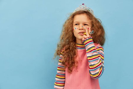 Téléchargez les photos : Stickers on face. Celebration. Little cute girl, child with curly hair posing in pink dress over blue studio background. Concept of childhood, emotions, fun, fashion, lifestyle, facial expression - en image libre de droit