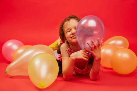 Photo for Little happy cute girl, child with curly hair posing with air balloons over bright red studio background. Concept of childhood, emotions, fun, fashion, lifestyle, facial expression - Royalty Free Image