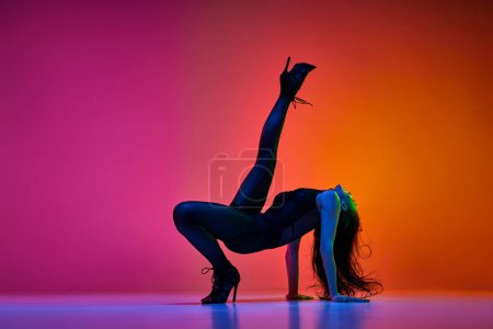 Téléchargez les photos : Flexibilité. Jeune femme, danseuse professionnelle exécutant la danse de talon haut sur fond de studio rose rouge dégradé dans la lumière néon. Concept de danse contemporaine style, art, esthétique, passe-temps, créativité - en image libre de droit