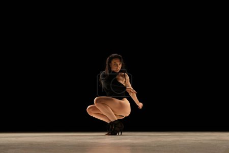 Téléchargez les photos : Sensuality and femininity. Young woman in bodysuit and heels dancing, performing over black background. Concept of contemporary dance style, art, aesthetics, hobby, creative lifestyle - en image libre de droit