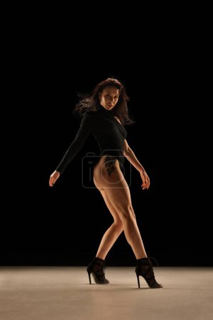 Téléchargez les photos : Step by step. Young woman in bodysuit and heels dancing, performing over black background. Concept of contemporary dance style, art, aesthetics, hobby, creative lifestyle, emotions - en image libre de droit