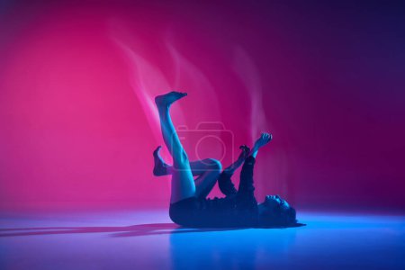 Téléchargez les photos : Inner world. Young talented woman dancing, performing over gradient pink studio background in neon with mixed lights. Concept of contemporary dance style, art, aesthetics, hobby, creative lifestyle - en image libre de droit