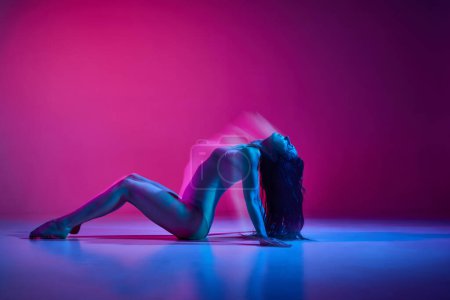 Foto de Young flexible woman in bodysuit performing contemp over gradient pink studio background in neon with mixed lights. Concept of contemporary dance style, art, aesthetics, hobby, creative lifestyle - Imagen libre de derechos