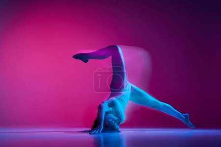 Foto de Dynamic portrait of young flexible woman dancing contemp, freestyle dance on gradient pink studio background in neon with mixed lights. Concept of contemporary dance style, art, aesthetics, creativity - Imagen libre de derechos