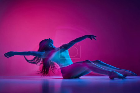 Téléchargez les photos : Self-love. Freestyle. Young woman dancing in bodysuit over gradient pink studio background in neon with mixed lights. Concept of contemporary dance style, art, aesthetics, hobby, creative lifestyle - en image libre de droit