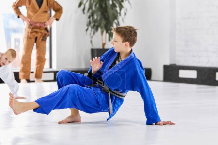 Photo for Boy, child in blue uniform, kimono training judo, jiu-jitsu with coach indoors. Active lifestyle. Popular hobby. Concept of martial arts, combat sport, sport education, childhood, - Royalty Free Image