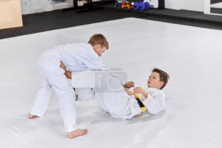 Photo for Two boys, children in white kimono training judo, jiu-jitsu fight style indoors. Developing strength and sportive knowledges. Concept of martial arts, combat sport, sport education, childhood, - Royalty Free Image