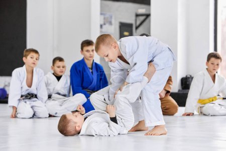 Foto de Niños pequeños, niños en kimono blanco entrenando judo, jiu-jitsu en interiores. Club deportivo profesional para niños. Concepto de artes marciales, deporte de combate, educación deportiva, infancia, hobby - Imagen libre de derechos