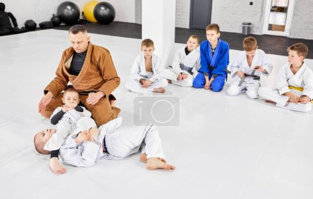 Foto de Boys, children in white kimono training judo, jiu-jitsu fight style indoors with coach. Developing strength and endurance. Concept of martial arts, combat sport, sport education, childhood, - Imagen libre de derechos