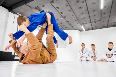Photo for Teacher, professional judo, jiu jitsu coach training kinds, boys, showing exercises. Children learning indoors. Concept of martial arts, combat sport, sport education, childhood, hobby - Royalty Free Image