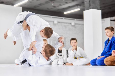 Foto de Retrato dinámico. Niños, niños en entrenamiento de kimono blanco, practicando judo, ejercicios de jiu-jitsu en interiores. ¡Atención! Concepto de artes marciales, deporte de combate, educación deportiva, infancia, - Imagen libre de derechos