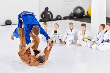 Photo for Teacher, professional judo, jiu jitsu coach training kinds, boys, showing exercises. Children attentively looking. Concept of martial arts, combat sport, sport education, childhood, hobby - Royalty Free Image