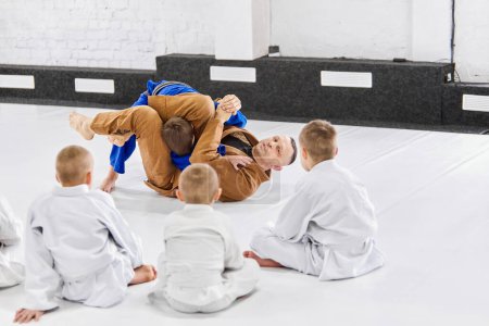 Photo for Teacher, professional judo, jiu jitsu coach training kinds, boys, showing exercises. Children learning indoors. Attentive kids. Concept of martial arts, combat sport, sport education, childhood - Royalty Free Image