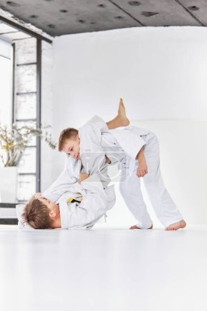 Foto de Professional exercises. Boys, children in white kimono training, practising judo, jiu-jitsu exercises indoors. Concept of martial arts, combat sport, sport education, childhood, hobby - Imagen libre de derechos