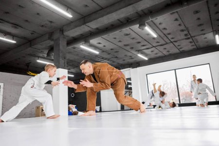 Foto de Retrato dinámico del hombre, judo profesional, entrenamiento de entrenador jiu-jitsu con niño pequeño, niño en kimono blanco. Niños haciendo ejercicios. Concepto de artes marciales, deporte de combate, educación deportiva, infancia - Imagen libre de derechos