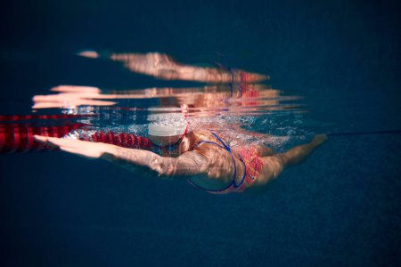 Photo for Growing speed and strength. Young woman, professional swimmer in goggles and cap training in swimming pool. Underwater view. Concept of sport, endurance, competition, energy, healthy lifestyle - Royalty Free Image