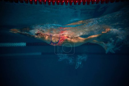 Foto de Bubbles. Professional female swimmer in cap and goggles in motion, training in swimming pool indoor. Underwater view. Concept of sport, endurance, competition, energy, healthy lifestyle - Imagen libre de derechos