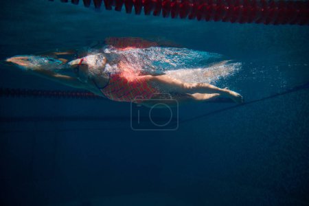 Foto de Side view. Strong sportive woman, professional swimmer training in swimming pool indoor. Athlete in goggles and cap. Underwater view. Sport, endurance, competition, energy, healthy lifestyle concept - Imagen libre de derechos