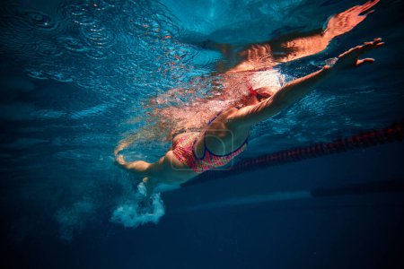 Téléchargez les photos : Muscular athlete. Competitive woman, professional female swimmer training in swimming pool indoor. Underwater view. Concept of sport, endurance, competition, energy, healthy lifestyle - en image libre de droit