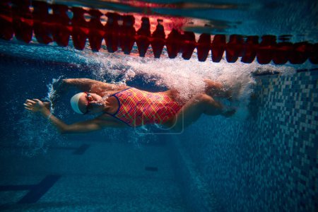 Foto de Start of move. Sportive woman, professional swimmer training in swimming pool indoor. Athlete in goggles and cap. Underwater view. Concept of sport, endurance, competition, energy, healthy lifestyle - Imagen libre de derechos