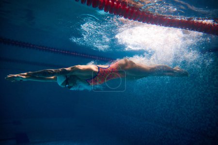 Téléchargez les photos : Developing speed. Professional female swimmer training in swimming pool indoor. Underwater view. Concept of sport, endurance, competition, energy, healthy lifestyle, power and strength - en image libre de droit