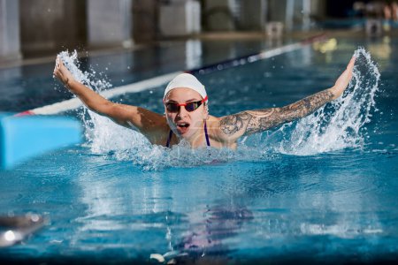 Téléchargez les photos : Butterfly swimming type. Young woman, professional female swimming athlete in cap and goggles training in pool indoors. Concept of sport, endurance, competition, energy, healthy lifestyle - en image libre de droit