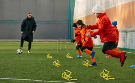Foto de Fast movements. Boys, children, football players doing exercises, warming up before training session with coach on sports field outdoors. Sport, childhood, active lifestyle, hobby, sport club concept - Imagen libre de derechos
