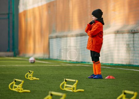 Photo for Little boy, child, football player in uniform standing on sports field near equipment for warming up activity. Concept of sport, childhood, active lifestyle, hobby, sport club - Royalty Free Image