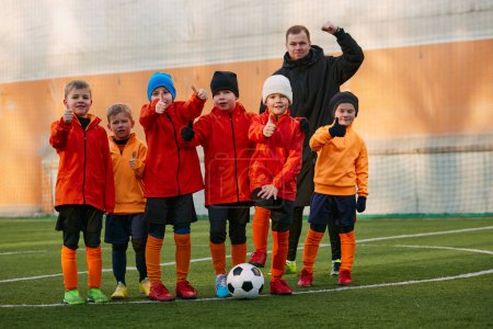 Téléchargez les photos : Group of boys, children, football players in uniform standing in a line on sports field grass outdoor, posing with coach. Concept of sport, childhood, active lifestyle, hobby, sport club - en image libre de droit