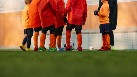 Foto de Cropped image of male legs on grass of sports field outdoors. Children playing football with coach. Concept of sport, childhood, active lifestyle, hobby, sport club - Imagen libre de derechos