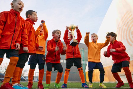 Photo for Winning emotions. Group of little boys, children in uniform, football players raising award, trophy. Kids training on outdoor playground. Sport, childhood, active lifestyle, hobby, sport club concept - Royalty Free Image