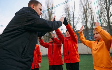 Téléchargez les photos : Professional football coach giving high five, cheering kids football team on field outdoor. Successful game. Concept of sport, childhood, active lifestyle, hobby, sport club - en image libre de droit