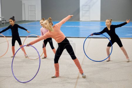 Competition preparation. Little girls, children, rhythmic gymnasts training indoors, doing exercise with hoop. Concept of sportive lifestyle, childhood, education, professional sport, championship