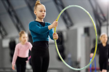 Photo for Concentration. Little girl, child, rhythmic gymnast training indoors, doing exercise with hoop. Concept of sportive lifestyle, childhood, education, health, professional sport and championship - Royalty Free Image